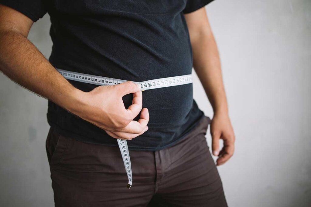 a man holds a measuring tape around his belly