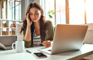 person looking away from laptop screen while dealing with a headache and wondering about reducing migraines with nad